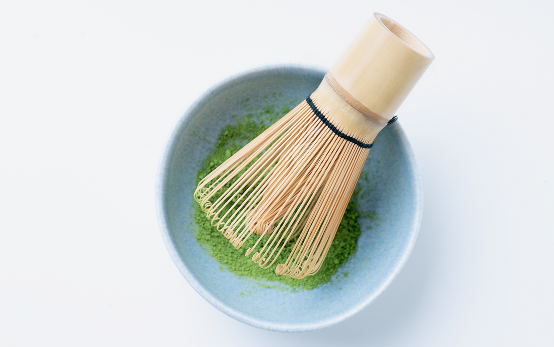 A bamboo matcha whisk in a bowl of matcha powder