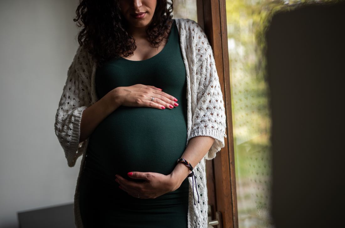 A pregnant woman in a green dress holding her belly lovingly.