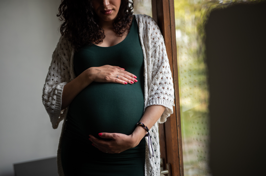 A pregnant woman in a green dress holding her belly lovingly. 